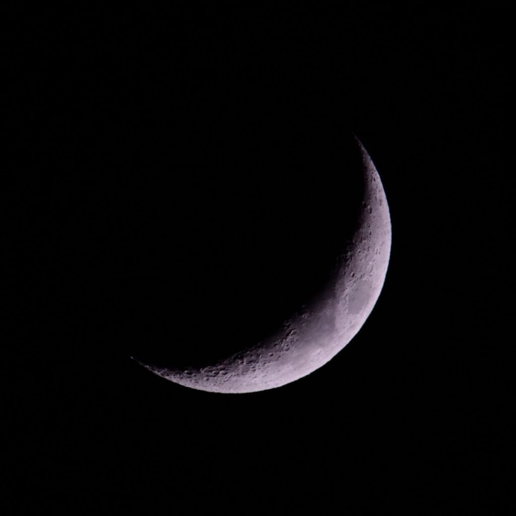 A crescent moon shines brightly in the night sky.